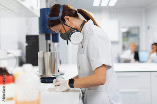 Mature female pharmaceutical technician writing data at desk in laboratory