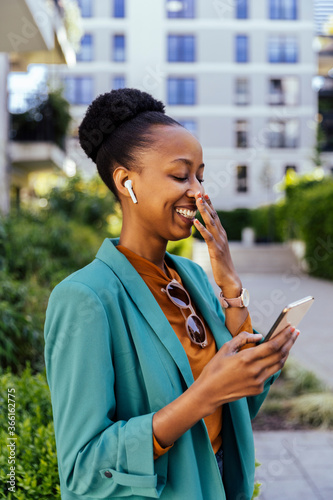 Laughing businesswoman using her smartphone and earpods outdoors photo