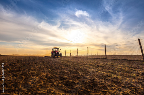 Farmer in tractor plowing agricultural land against cloudy sky