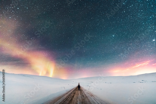 Man standing on country road under starry sky with northern lights, Lebesby, Norway