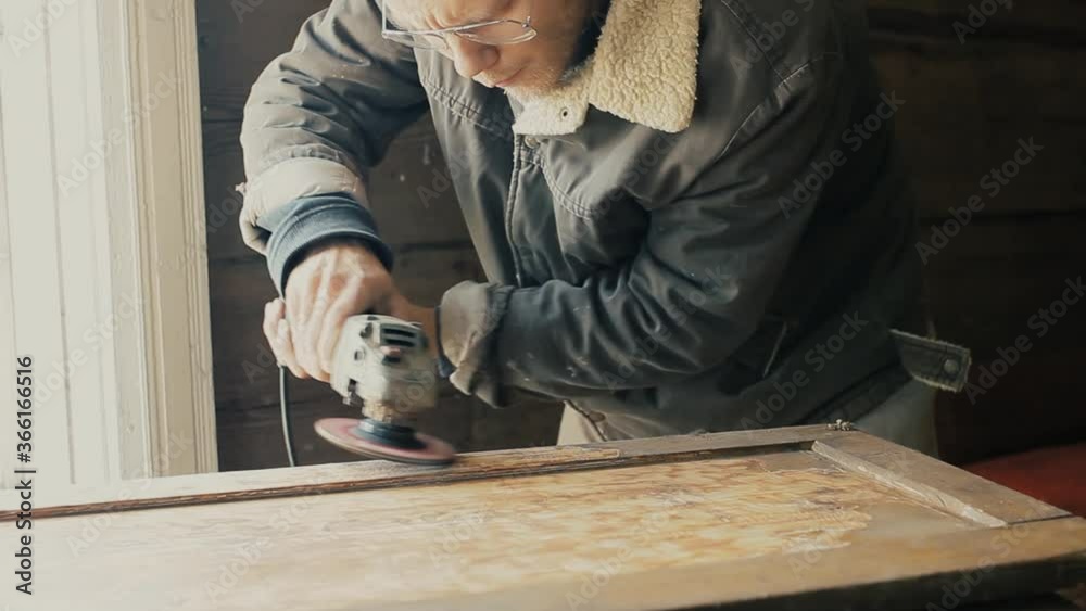 male artisan grinds a wooden board, cabinet door with an electric grinder. Furniture restoration.