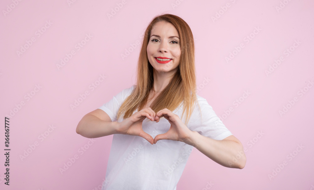 Picture of cheerful beautiful charismatic female looking directly at camera, making gesture, showing shape of heart with two hands, having pleasant facial expression, feeling love. Mood concept.
