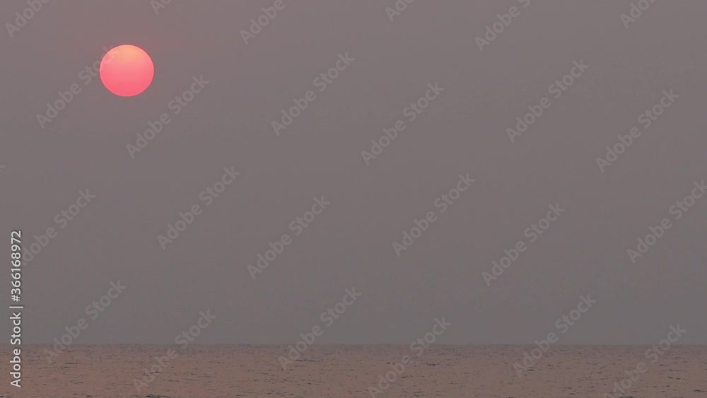 Red and yellow sun above the sea partly hiding in clouds on grey sky background. Hot summer season weather, close up big sun and ray. Sunset, timelapse.
Red and yellow sun above the sea partly hiding in clouds on grey sky background. Hot summer season weather, close up big sun and ray. Sunset, timelapse.