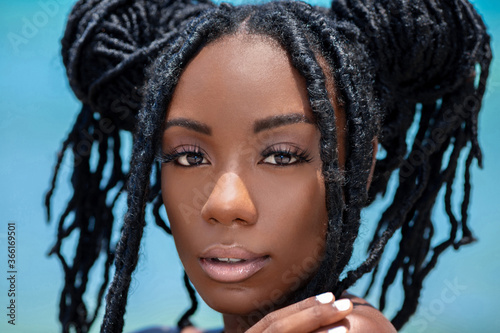Headshot of a sensual looking attractive young black female with beautiful makeup & long dreadlocks posing by herself on a sunny summer day at a tropical beach. photo
