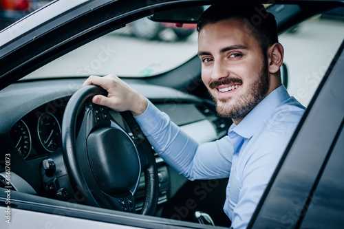 joyful and handsome looking man sitting in a luxury car posing