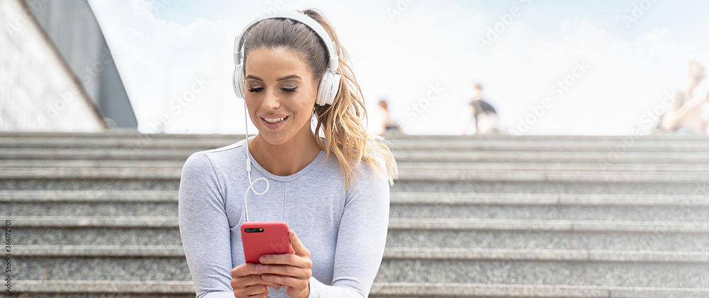 Obraz premium Fit smiling girl listening music on the city street.