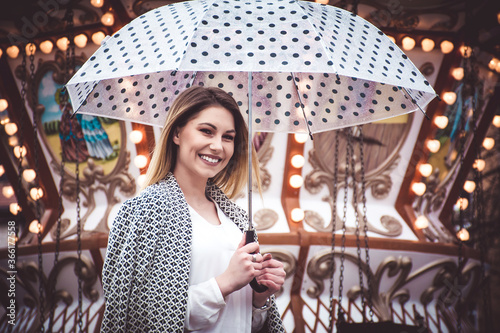 joyful young woman holding her umbrella and enjoying her time at a carnival 