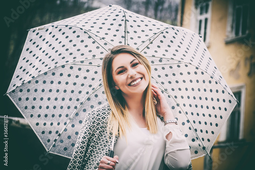Woman laughing while holding her umbrella and fixing her hair outdoors