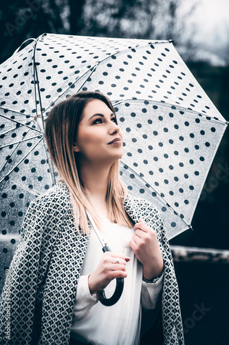 young woman daydreaming and standing under an umbrella outdoors