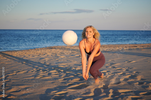 Stunning young blonde woman poses on beach in work-out attire with volleyball - dig