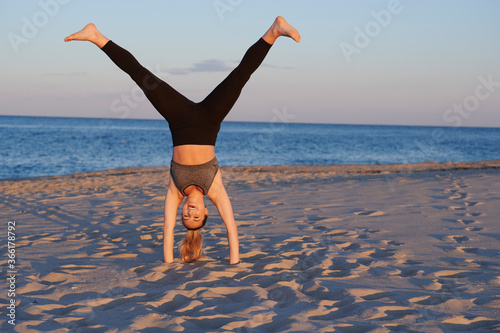 Stunning young blonde woman working out on beach at sunset - handstand walk-over