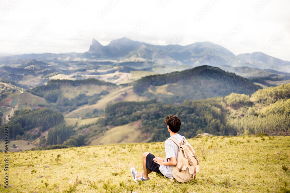 Young adventurous traveler sitting on top of a mountain carrying a backpack and admiring the mountains of the State of Espirito Santo, Brazil. 