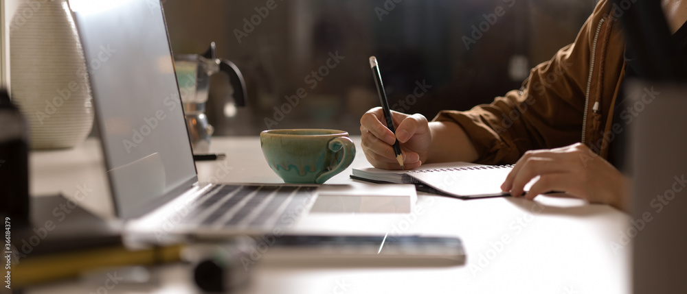 Female taking note on blank schedule book on white table with mock up laptop and supplies in studio