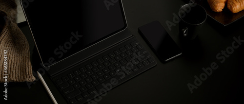 Dark home office with croissants, coffee up, digital tablet, smartphone and supplies on black desk