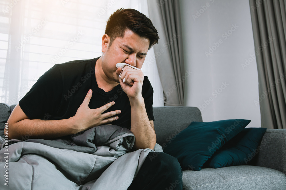 Asian people are sick or ill with bronchitis while coughing by covering their mouth with tissue paper when he sit on the sofa at home. Asian people are sick or ill with bronchitis while coughing by covering their mouth with tissue paper when he sit on the sofa at home.