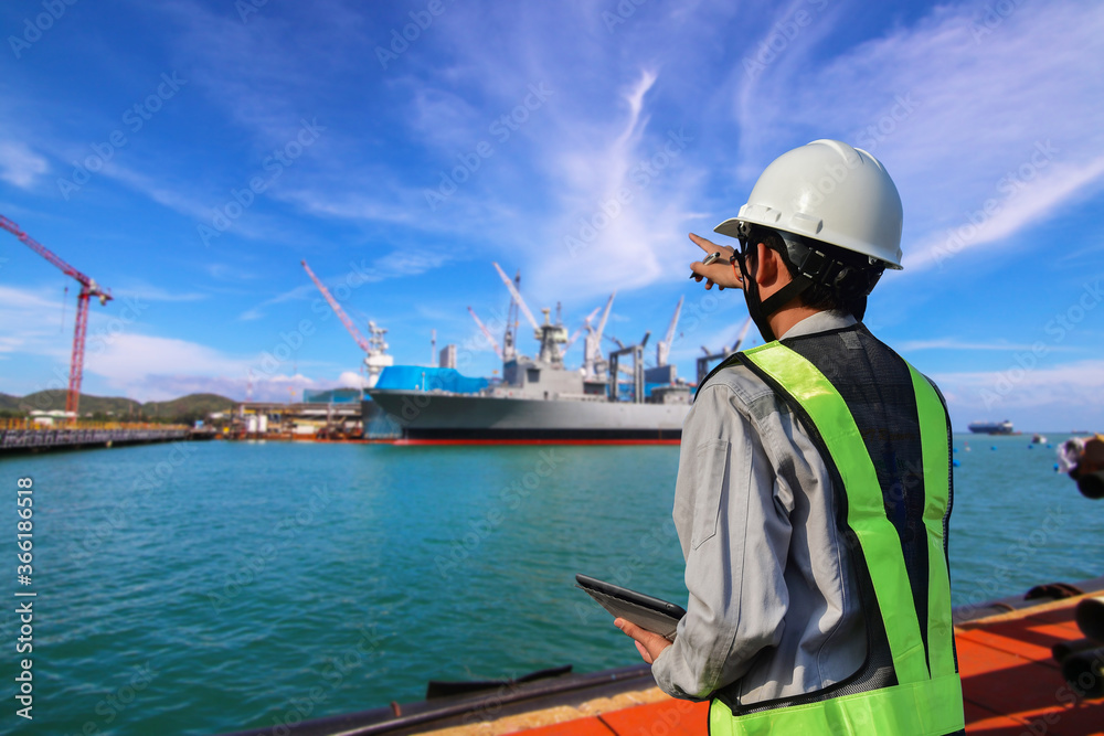 workers with tablet and Pointing at the target during the operation of ship in shipyard ship moored alongside near floating dock yard on blue sky workers with tablet and Pointing at the target during the operation of ship in shipyard ship moored alongside near floating dock yard on blue sky