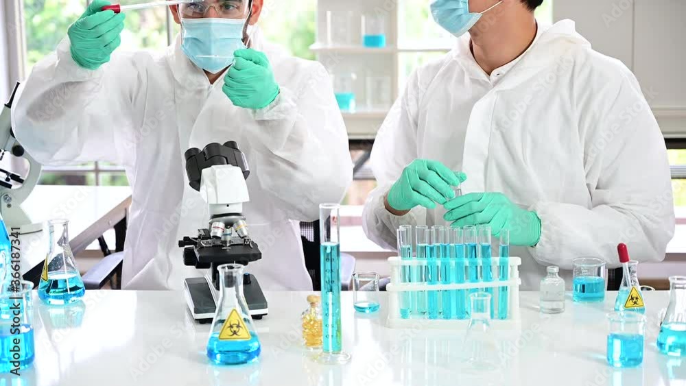 Couple male scientist wearing protection suit holding vaccine and working with many lab equipment for research vaccine at laboratory. Medical researcher specialist. Couple male scientist wearing protection suit holding vaccine and working with many lab equipment for research vaccine at laboratory. Medical researcher specialist.