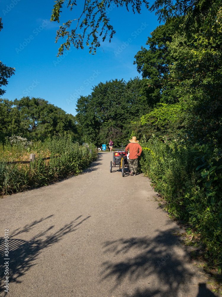 street vendor with floppy hat walking bicycle on tree-lined path