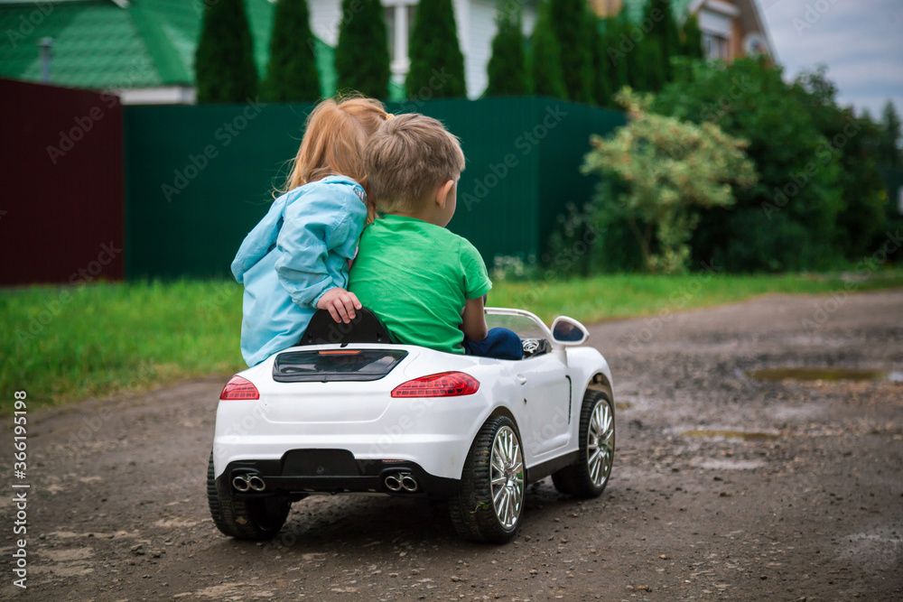 Little girl and boy riding a toy car.
