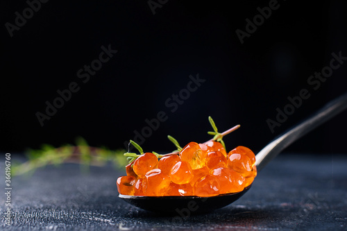 Salmon caviar in glass plate with spoon and ice on black background. Seafood