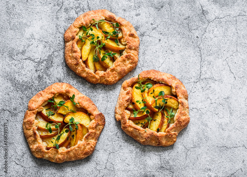 Ripe peaches, fresh thyme mini pies galettes - delicious summer pastry dessert on a grey background, top view