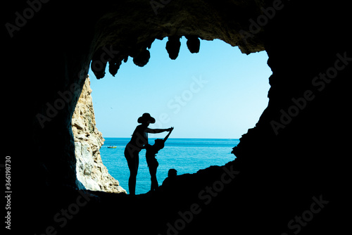 Mamma e figlia in silhouette dentro uina  grotta si divertono. Dietro il cielo e il mare del Cilento in Italia