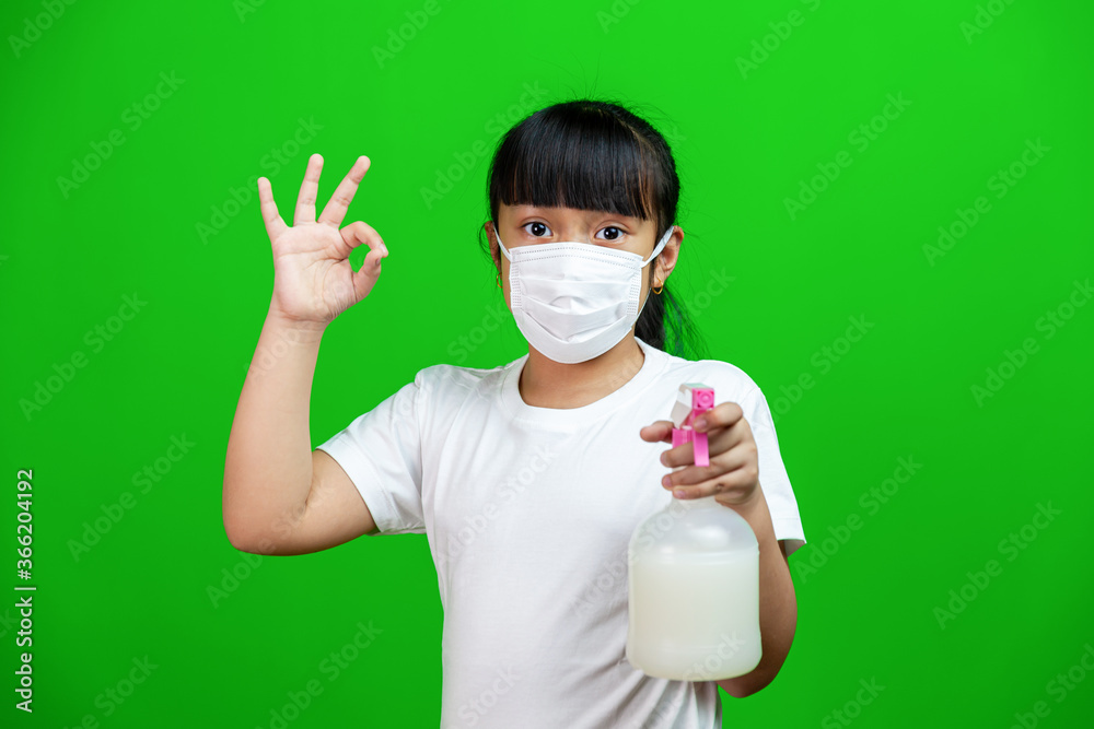Asian Girl wearing face mask to protect from COVID-19. she hold germicidal spray and standing on green background Asian Girl wearing face mask to protect from COVID-19. she hold germicidal spray and standing on green background