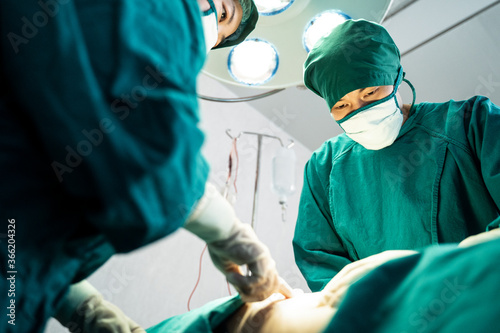 Professional medical team performing surgical operation in modern operating room. Asian assistant hands out instruments to surgeons doctor during operation on intensive care patient in hospital.