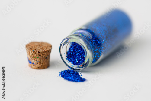 party, decoration and holidays concept - close up of ultramarine blue glitters poured from small glass bottle and cork stopper over white background