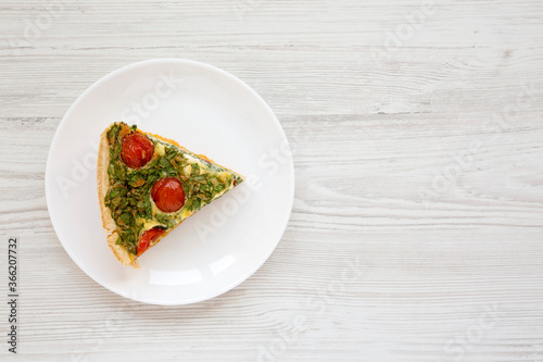 A Piece of Homemade Spinach Quiche on a white plate on a white wooden background, top view. Flat lay, overhead, from above. Space for text.