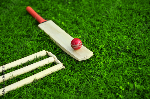 cricket set bat ball stumps and bails on green grass pitch background