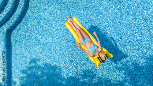 Beautiful young girl relaxing in swimming pool, woman swims on inflatable mattress and has fun in water on family vacation, tropical holiday resort, aerial drone view from above 