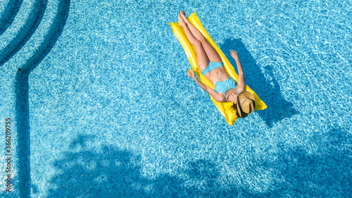 Beautiful young girl relaxing in swimming pool, woman swims on inflatable mattress and has fun in water on family vacation, tropical holiday resort, aerial drone view from above 