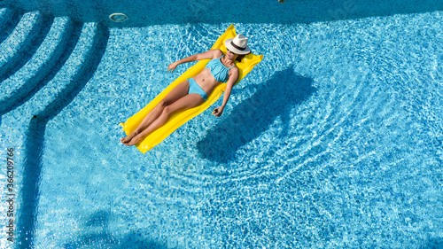 Beautiful young girl relaxing in swimming pool, woman swims on inflatable mattress and has fun in water on family vacation, tropical holiday resort, aerial drone view from above 