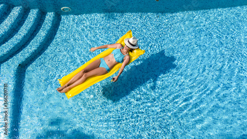 Beautiful young girl relaxing in swimming pool, woman swims on inflatable mattress and has fun in water on family vacation, tropical holiday resort, aerial drone view from above 