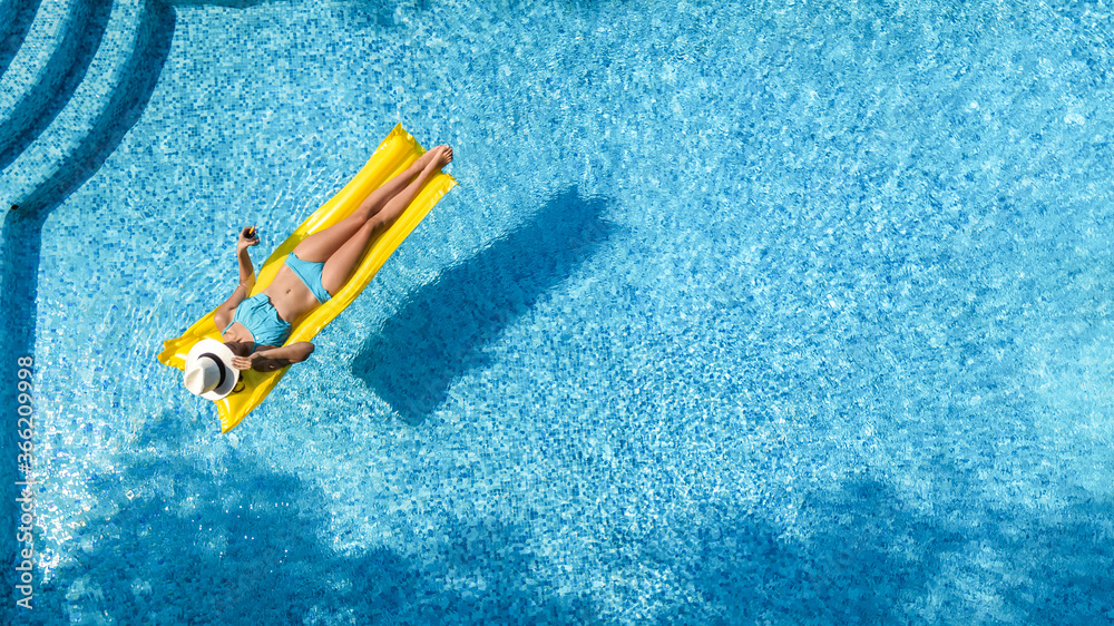 Beautiful young girl relaxing in swimming pool, woman swims on inflatable mattress and has fun in water on family vacation, tropical holiday resort, aerial drone view from above
