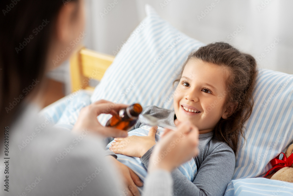 family, health and medicine concept - mother pouring cough syrup for little sick daughter lying in bed at home - obrazy, fototapety, plakaty 
