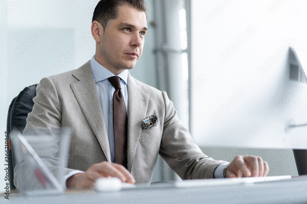 Fototapeta premium Young employee looking at computer monitor during working day in office
