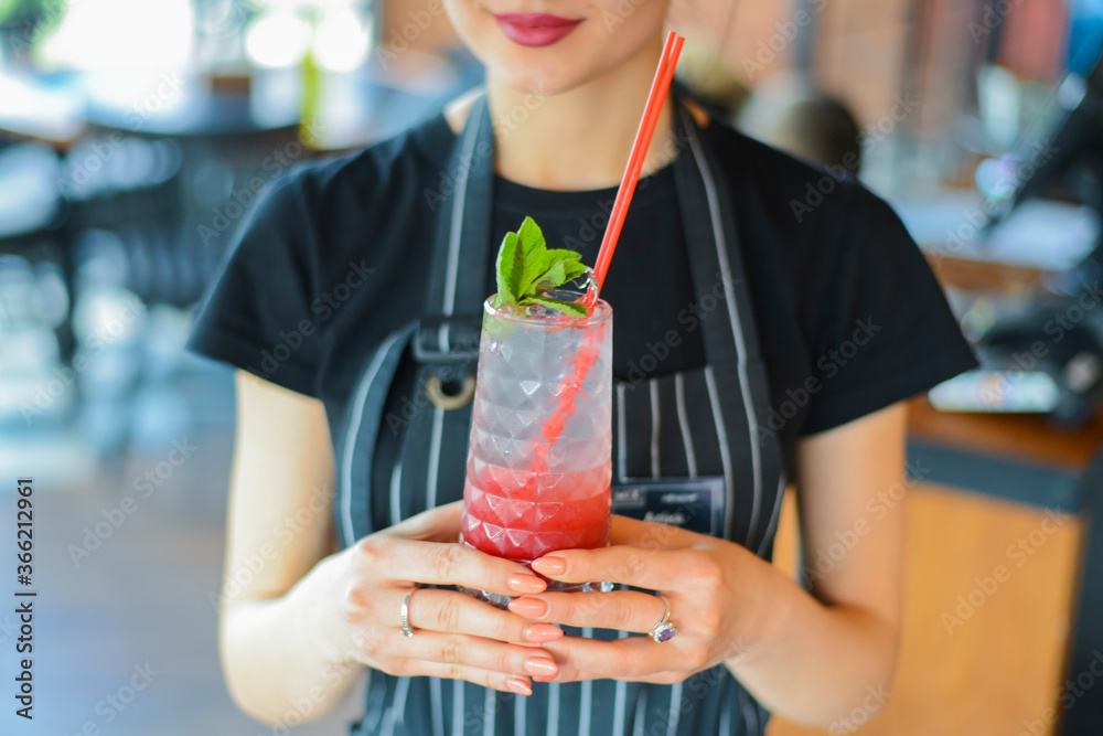 Fototapeta premium Attractive young woman waiter holding red colorful refreshing cocktail with ice and lime. Fruit tropical mix drink.