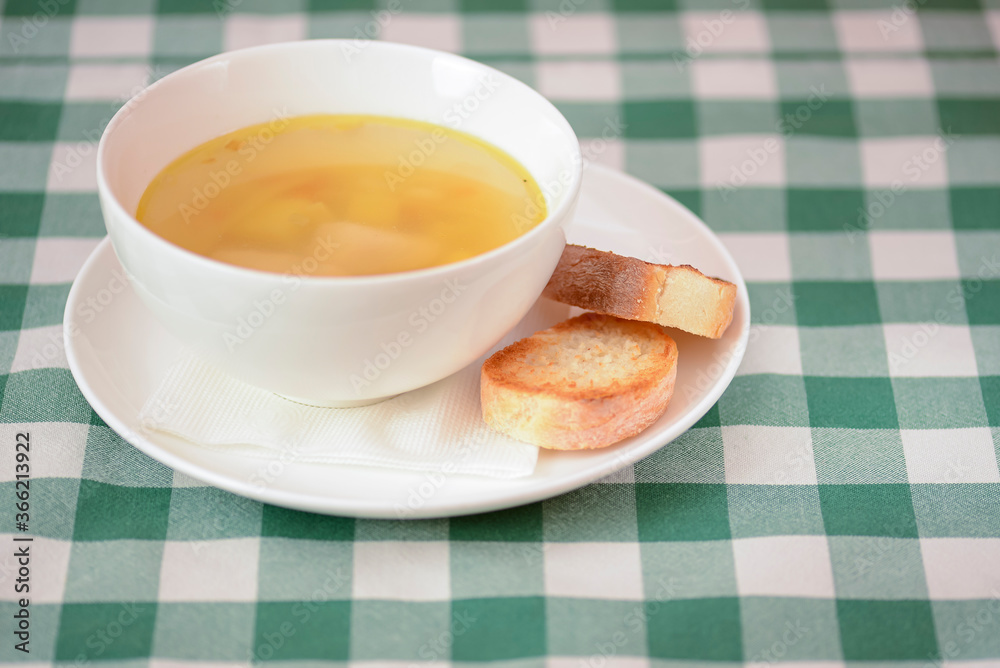 Chicken soup with vegetables and meat served in a white bowl over rustic wooden background with green plaid tablecloth. Chicken soup with vegetables and meat served in a white bowl over rustic wooden background with green plaid tablecloth.