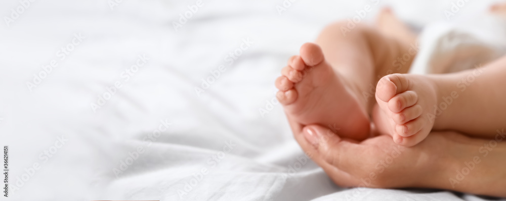 Mother holding feet of her little baby on bed, space for text. Banner design - obrazy, fototapety, plakaty 