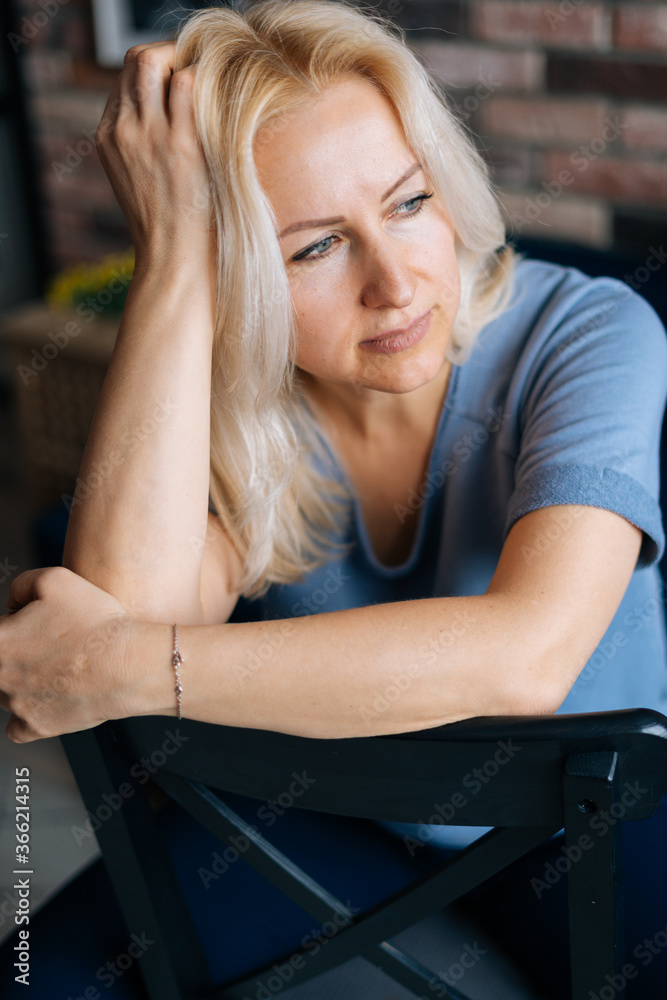 Close-up of face of blonde middle aged woman with perfect skin looking away. Portrait of lovely middle aged lady indoor.