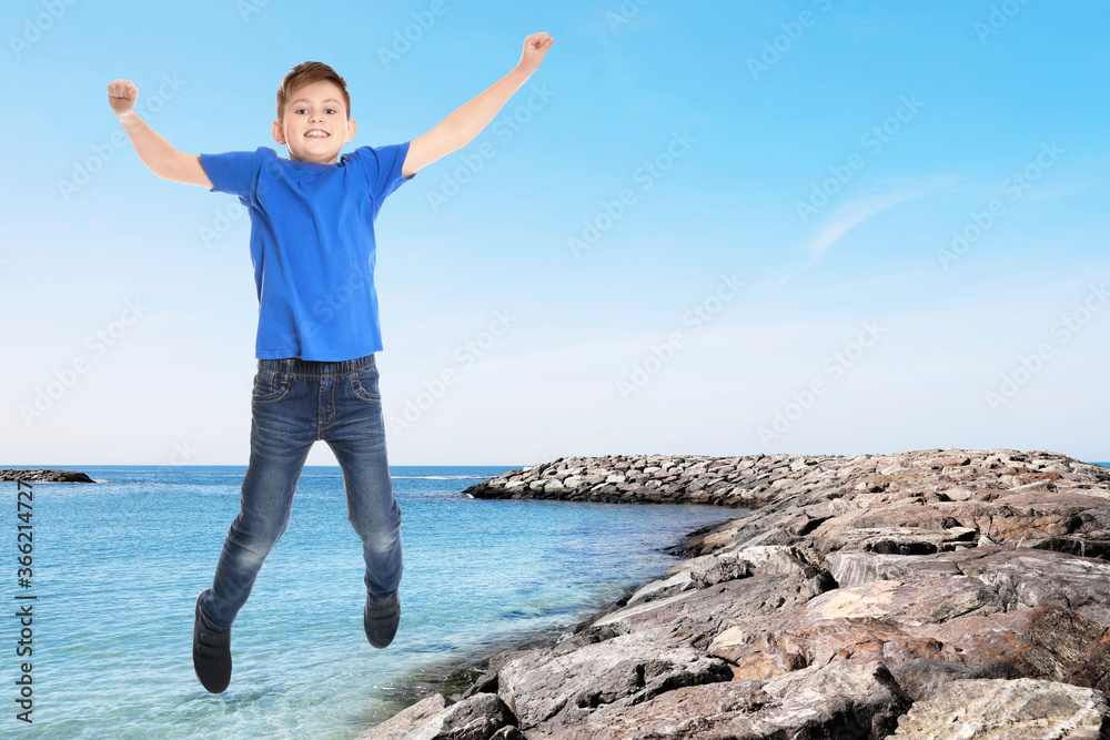 Cute school boy jumping on beach near sea, space for text. Summer holidays Cute school boy jumping on beach near sea, space for text. Summer holidays