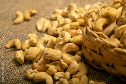 Cashew nuts in a wicker basket and cashew nuts scattered on burlap with a rough texture surface texture. Close up.
