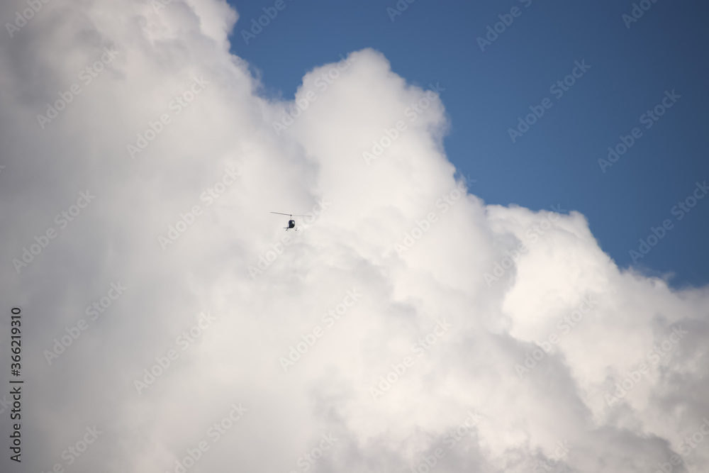 A small helicopter flies against the background of a large heaped cloud and blue sky in the style of minimalism A small helicopter flies against the background of a large heaped cloud and blue sky in the style of minimalism