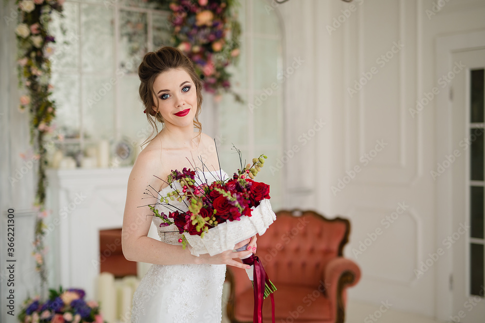 portrait of a beautiful young woman bride in a white dress with a red bouquet of roses in her hands