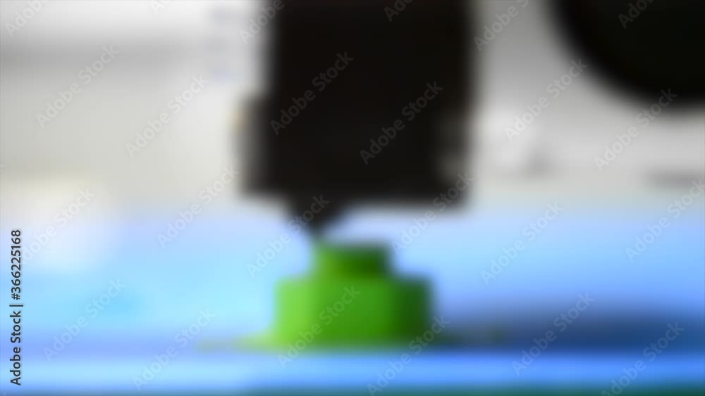 Blurred background. 3D printer prints green shape of plastic layers close-up Blurred background. 3D printer prints green shape of plastic layers close-up