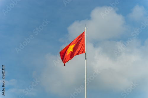 Red flag with yellow star, blue sky with clouds in background. Rippled texture. National flag of Vietnam. Popular country for tourism. Famous tourist destination