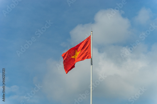 Red flag with yellow star, blue sky with clouds in background. Rippled texture. National flag of Vietnam. Popular country for tourism. Famous tourist destination