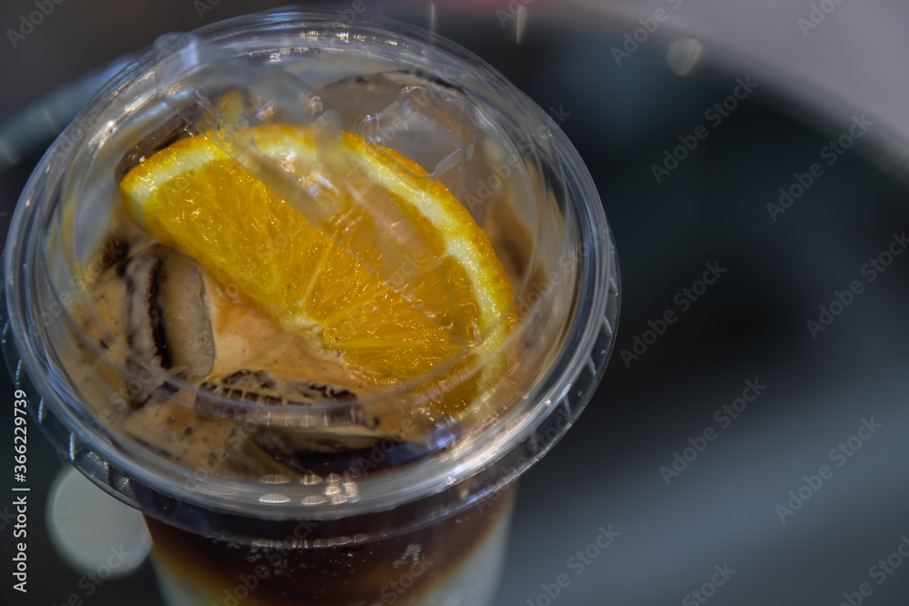 Iced coffee with orange or Yuzu Espresso Tonic - Close-up A plastic glass of espresso mixed with tonic and yuzu orange juice on blurred background, Refreshing summer drink concept. Selective focus. Iced coffee with orange or Yuzu Espresso Tonic - Close-up A plastic glass of espresso mixed with tonic and yuzu orange juice on blurred background, Refreshing summer drink concept. Selective focus.